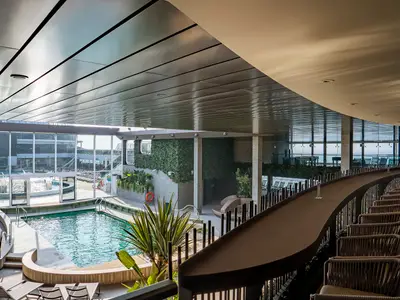Blick auf den hellen Botanic Garden Poolbereich der MSC World Europa. Ein großer Pool, Liegeflächen, begrünte Wände und eine lange, geschwungene Bar laden zum Entspannen ein.