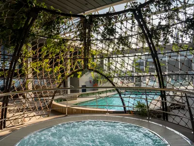 Ein sprudelnder Whirlpool im Vordergrund, dahinter der Botanic Garden Poolbereich mit grünen Pflanzen und Tageslicht an Bord der MSC World Europa.