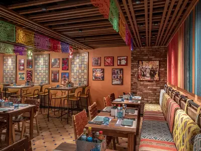 Innenansicht des farbenfrohen Spezialitätenrestaurants HOLA! Tacos & Cantina an Bord der MSC World Europa, mit rustikalen Holztischen, gelben Stühlen, gemusterten Fliesenwänden, farbigen Textilien und mexikanischer Deko. Ohne Personen.