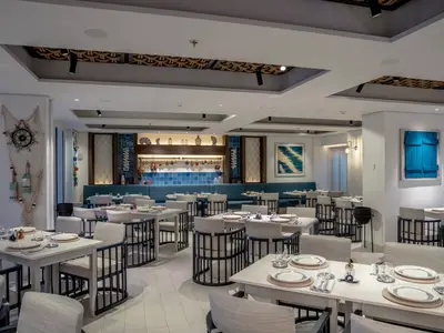 Geräumiges, maritim gestaltetes Spezialitätenrestaurant La Pescaderia an Bord der MSC World Europa, mit gedeckten Tischen, Stühlen und blauer Wandverkleidung.