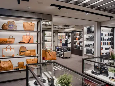 Ein heller, moderner Luxus-Shop mit Regalen voller MCM-Handtaschen, Rucksäcke und Geldbörsen an Bord der MSC World Europa. Ein Mannequin präsentiert ein Kleid in der Mitte.