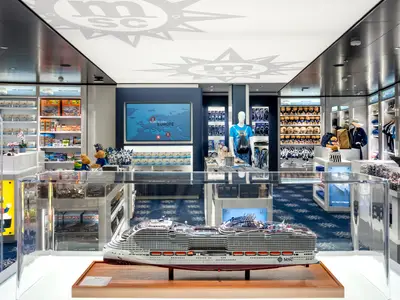 Heller MSC Shop an Bord der MSC World Europa. Regale voll mit Merchandise, Spielzeug und Kleidung. Im Vordergrund ein grosses Schiffsmodell. Ein Bildschirm zeigt eine Europakarte.