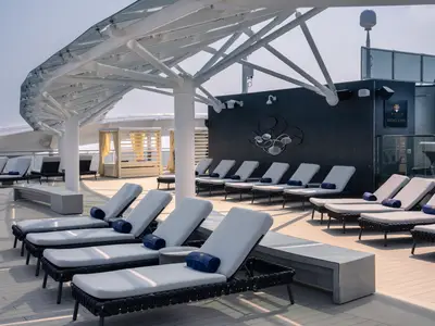 Luxuriöses Sonnendeck des MSC Yacht Clubs auf der MSC World Europa. Moderne Liegen, blaue Handtücher, Cabana und Poolbereich unter Glas-Metall-Überdachung.