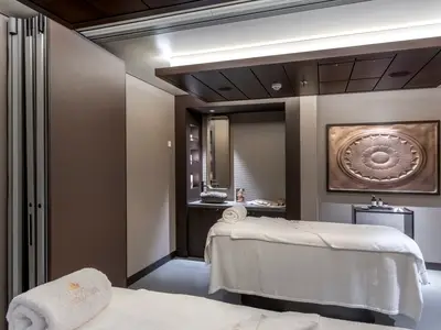 Ein Behandlungsraum im MSC Aurea Spa der MSC World Europa mit Massageliege, Waschbecken aus Stein und dekorativer Wandkunst.