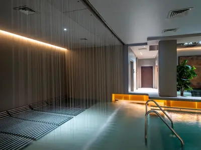 Modernes Spa an Bord der MSC World Europa. Großer Pool mit Regen-Wasservorhang, Liegeflächen und Akzentbeleuchtung. Entspannende Atmosphäre.