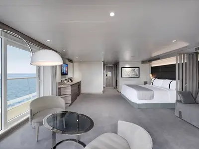 Geräumige Grand Suite an Bord der MSC World Europa. Die moderne Einrichtung mit großem Bett, Sofa, Sesseln und Balkon bietet direkten Meerblick.