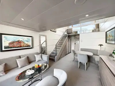 Innenansicht einer geräumigen, modernen Duplex-Suite an Bord der MSC World Europa. Im Vordergrund ein Wohnbereich mit Sofa, Couchtisch und Essbereich. Eine elegante Treppe führt in die obere Etage.