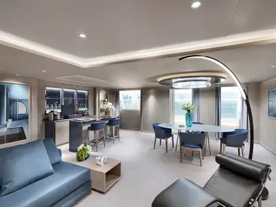 Eine elegante Owner's Suite an Bord der MSC World Europa mit blauen Sofas, einem Esstisch mit blauen Stühlen, einer voll ausgestatteten Bar und großen Fenstern mit Meerblick.