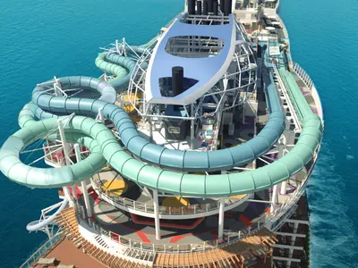 Rendering: Vogelperspektive auf die blauen und grünen Wasserrutschen des AquaPark am Bug der Norwegian Aqua. Die Bahnen schlängeln sich über das Deck und das türkisblaue Meer.