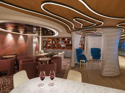 Blick in die moderne Swirl Wine Bar an Bord der Norwegian Aqua. Der Raum besticht durch eine gewellte Holzdecke mit leuchtenden LED-Linien und vertikal beleuchtete Säulen. Verschiedene Sitzbereiche mit roten und blauen Sesseln sowie ein Bücherregal laden zum Verweilen ein.