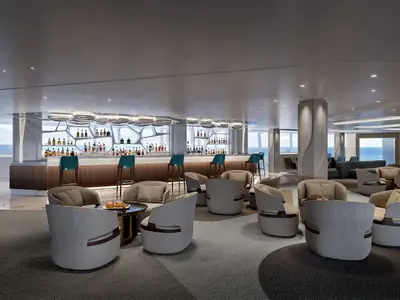 Detailaufnahme der modernen Belvedere Bar an Bord der Norwegian Aqua, die stilvolle Lounge-Sessel und eine lange Bar mit leuchtenden Flaschenregalen vor großen Fenstern mit Meerblick zeigt.