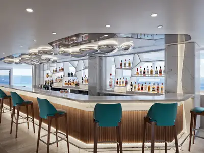 Moderne Belvedere Bar an Bord der Norwegian Aqua. Beleuchtete Theke mit Hockern, Regale voller Spirituosen und große Fenster mit weitem Meerblick.