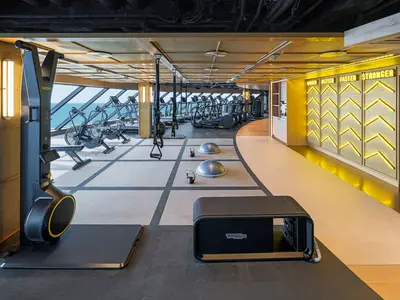 Das moderne Fitnesscenter der Norwegian Aqua bietet diverse Trainingsgeräte mit Panoramablick auf das Meer. Eine beleuchtete Wand mit Motivationssprüchen ist zu sehen.