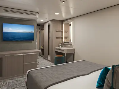 Moderne Innenkabine an Bord der Norwegian Aqua mit einem bequemen Bett, einem Flachbildfernseher, der eine Meeresansicht zeigt, einem Waschtisch mit beleuchtetem Schminkspiegel und einem Hocker.