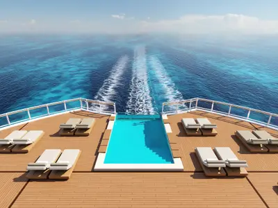 Das Heckdeck der Norwegian Aqua zeigt einen Infinity-Pool und mehrere moderne Liegestühle. Dahinter erstreckt sich das weite, blaue Meer mit der weissen Schiffspur.