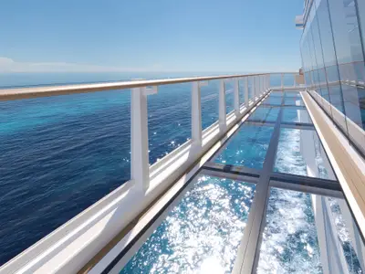 Blick über den Oceanwalk an Bord der Norwegian Aqua. Ein Glasbodenweg erstreckt sich über das tiefblaue Meer mit glitzernden Sonnenreflexionen, umgeben von einem weissen Geländer und der verglasten Schiffswand.