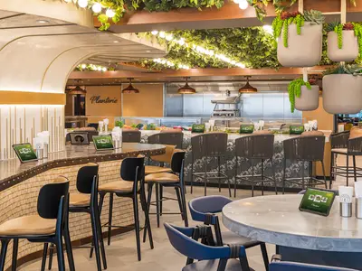 Modernes Restaurant 'Planterie' an Bord der Norwegian Aqua mit Theke, Barhockern, digitalen Menüs, frischen Speisen und Pflanzen an der Decke.