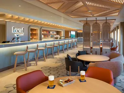 Eine geräumige Bar und Lounge 'The Local' an Bord der Norwegian Aqua mit einer langen Bar, Barhockern, Tischen und bequemen Sesseln, die zum Verweilen einladen.