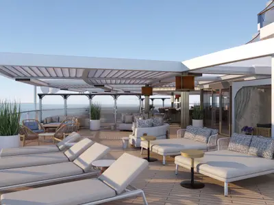 Eine moderne Outdoor-Lounge an Bord der Norwegian Aqua mit bequemen Liegen und Loungemöbeln unter einem stylischen Sonnendach und weitem Blick auf das Meer. Keine Personen sind sichtbar.