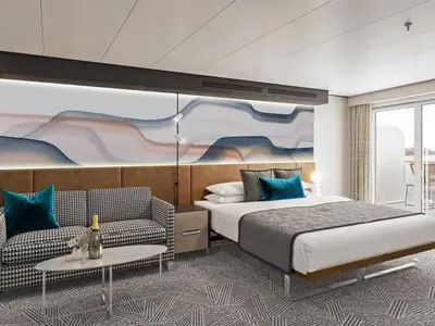 Helle, moderne Club Balcony Suite an Bord der Norwegian Aqua. Sie zeigt ein großes Bett, ein Sofa im Hahnentrittmuster, stilvolle Wandkunst, Teppichboden und einen Balkon mit Meerblick.