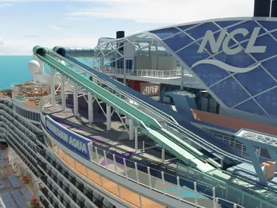 Obere Decks der Norwegian Aqua mit Blick auf den weitläufigen Wasserrutschen-Bereich und einem modernen Glasbau mit NCL-Logo. Das Schiff fährt auf dem tiefblauen Meer unter hellem Himmel.
