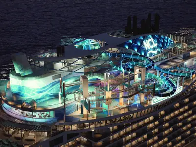 Nachtaufnahme eines Renderings der Norwegian Aura. Die oberen Decks sind lebhaft beleuchtet mit blauen Wasserrutschen, einem Hochseilgarten und einem Poolbereich, umgeben vom dunklen Meer.
