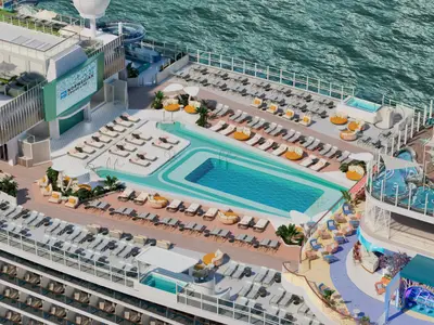 Vogelperspektive auf das weitläufige Pooldeck der Norwegian Aura mit einem grossen Hauptpool, zahlreichen Sonnenliegen und Loungebereichen in hellen Farben direkt am Meer.