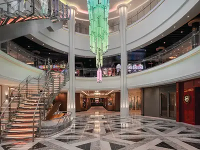 Atrium an Bord der Norwegian Bliss mit beleuchteter Glas-Wendeltreppe und farbwechselndem Kronleuchter. Spielautomaten im Obergeschoss, Kunstgalerie im Erdgeschoss.