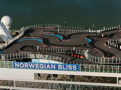 Vogelperspektive auf die Go-Kart-Rennstrecke auf dem Oberdeck der Norwegian Bliss. Mehrere Karts fahren auf der kurvigen Strecke, umgeben von Schutzbarrieren und dem weiten Meer im Hintergrund.