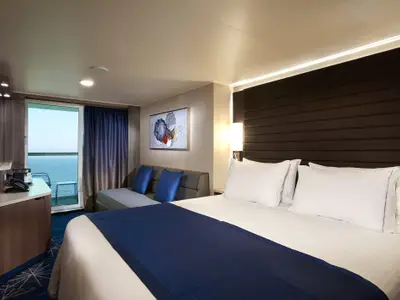 Geräumige Balkonkabine der Norwegian Bliss mit großem Bett, bequemer Couch und TV-Bereich. Im Hintergrund ein Balkon mit Meerblick.