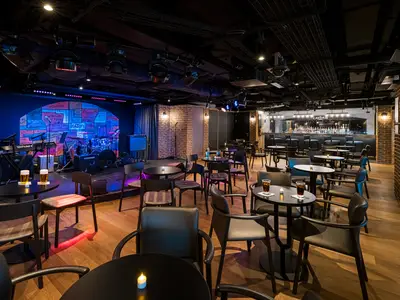Live-Musik-Club an Bord der Norwegian Bliss. Bühne mit Instrumenten links, Bar rechts. Viele Tische und Stühle. Ziegelwände und gedämpftes Licht.