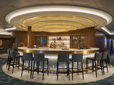 Elegante Atrium Bar an Bord der Norwegian Bliss. Eine kreisfoermige Bar mit dunklen Barhockern, gefuellten Regalen und goldener Deckenbeleuchtung. Modernes Interieur ohne Personen.