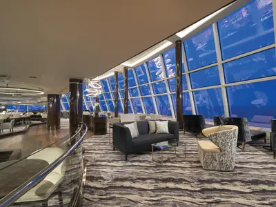 Moderne Observation Lounge an Bord der Norwegian Bliss mit blauen Fenstern und bequemen Sitzbereichen. Ein langer Bartresen und elegante Beleuchtung sind zu sehen.