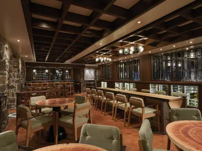 Die elegante Weinbar 'The Cellars' an Bord der Norwegian Bliss. Einladender Innenraum mit Steinwänden, dunklem Holz und modernen Leuchten. Weinkühler und diverse Sitzbereiche mit Tischen und Stühlen.