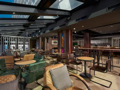 Moderne Bar-Lounge an Bord der Norwegian Bliss. Ledersessel, Holztische, eine lange Bar mit Bierhähnen. Glasdach und Fenster mit Meerblick.