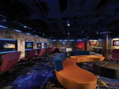 Bordunterhaltung auf der Norwegian Bliss: Eine moderne Lounge mit Gaming-Stationen, Foosball, Air-Hockey und komfortablen Sitzgelegenheiten. Blaue LED-Beleuchtung schafft eine lebendige Atmosphäre.