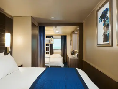 Eine helle Familien-Aussenkabine an Bord der Norwegian Bliss. Im Vordergrund ein Doppelbett, dahinter ein abgetrennter Bereich mit Kojenbetten und einem Fenster mit Meerblick.
