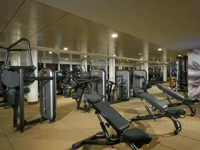 Modernes Fitnesscenter an Bord der Norwegian Bliss mit Technogym-Geräten wie Laufbändern und Hantelbänken auf hellem Boden. Keine Personen.