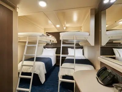 Eine geräumige Innenkabine auf der Norwegian Bliss mit zwei Einzelbetten am Boden und zwei oberen Klappbetten mit Leitern. Modernes Design mit blauen Akzenten und Holzelementen.