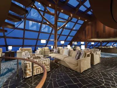 Blick in die elegante Haven Observation Lounge an Bord der Norwegian Bliss mit Baumstruktur, großen Fenstern und zahlreichen Sitzgelegenheiten.