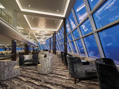 Die moderne Observation Lounge der Norwegian Bliss bietet komfortable Sitzgelegenheiten und große Panoramafenster mit Blick auf das Meer. Eine Treppe führt zu einer unteren Bar.