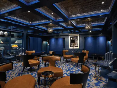 Eine luxuriöse Lounge in Blautönen an Bord der Norwegian Bliss. Der Raum ist mit bequemen Ledersesseln, Bücherregalen und markanten Deckenleuchten ausgestattet. Die einzigartigen Hand-Sessel setzen Akzente.