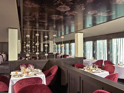 Das elegante Spezialitätenrestaurant Le Bistro an Bord der Norwegian Bliss mit roten Samtstühlen, fein gedeckten Tischen und floraler Decke.