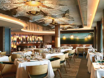 Elegantes Spezialitätenrestaurant Ocean Blue an Bord der Norwegian Bliss. Mit weiss gedeckten Tischen, modernen Stühlen und stilvollen Lichtinstallationen.