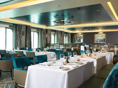 Elegantes Restaurant "Taste" an Bord der Norwegian Bliss. Weiss gedeckte Tische, tealblaue Stühle und Bänke. Grosse Fenster und moderne Deckenbeleuchtung prägen den Raum.