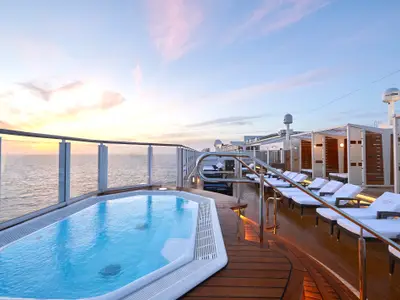 Sonnenuntergang über dem Meer, gesehen vom luxuriösen Sonnendeck The Haven der Norwegian Bliss, mit Pool, Liegestühlen und privaten Cabanas.