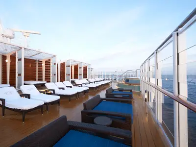 Blick auf das leere Haven Sonnendeck der Norwegian Bliss am frühen Morgen. Zahlreiche Sonnenliegen und bequeme Loungesessel stehen bereit. Im Hintergrund ist das Meer zu sehen.