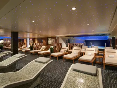 Ein ruhiger Spa-Bereich, die Thermal Suite an Bord der Norwegian Bliss. Zahlreiche Liegen stehen unter einem Sternenhimmel, im Hintergrund ist ein Pool zu sehen.