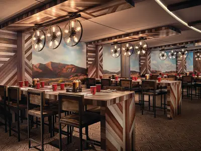 Rustikales Restaurant an Bord der Norwegian Bliss. Holztische, Barhocker, rote Becher, Bergwandbilder und Wagenrad-Kronleuchter prägen das Ambiente.