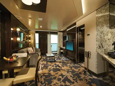 Ansicht einer eleganten Suite an Bord der Norwegian Bliss. Das Zimmer verfügt über einen Wohnbereich, Esstisch, Küchenzeile und Balkon mit Meerblick.